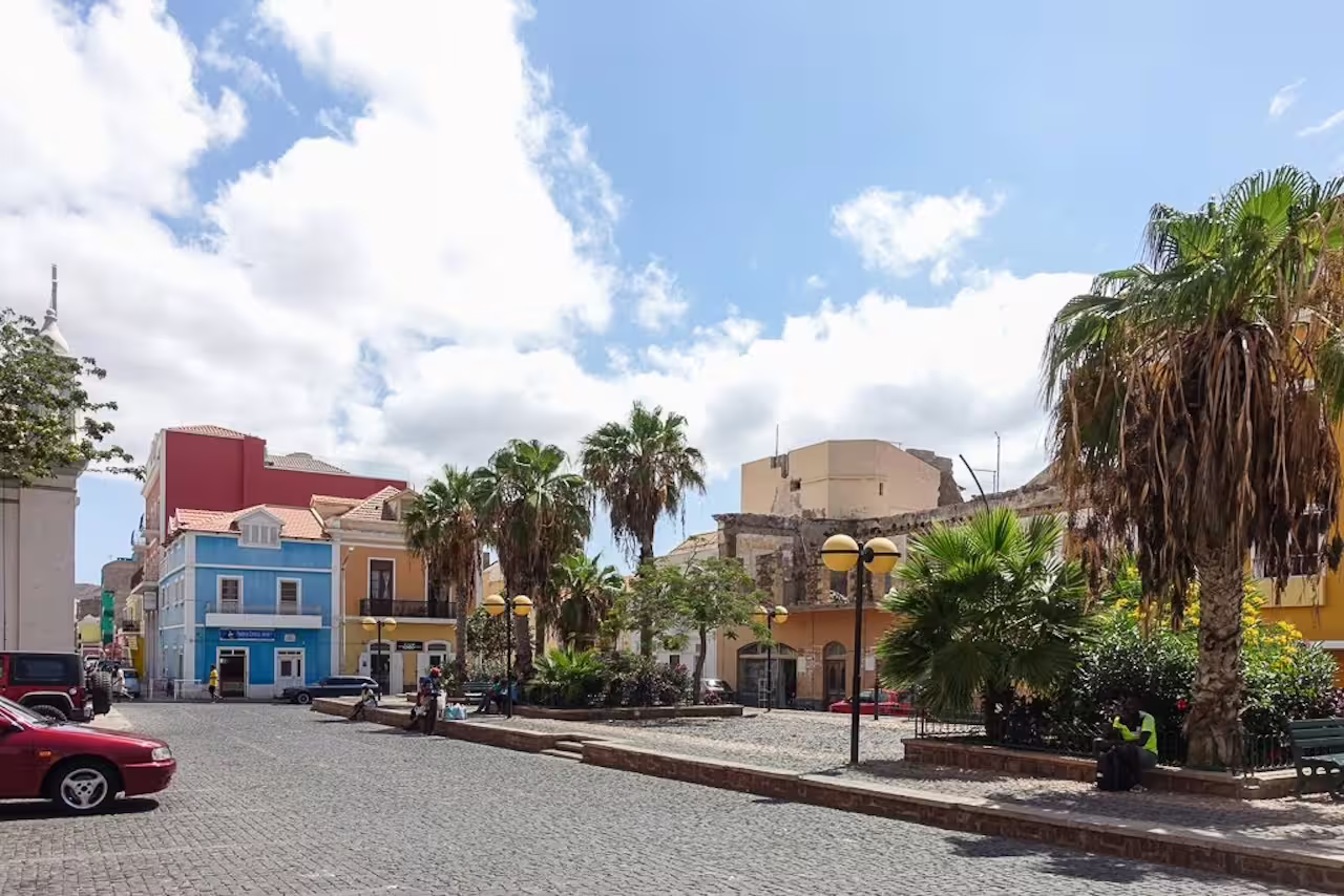Colorful colonial buildings and palm trees line a sunny cobblestone street in Mindelo, São Vicente, perfect for exploring.