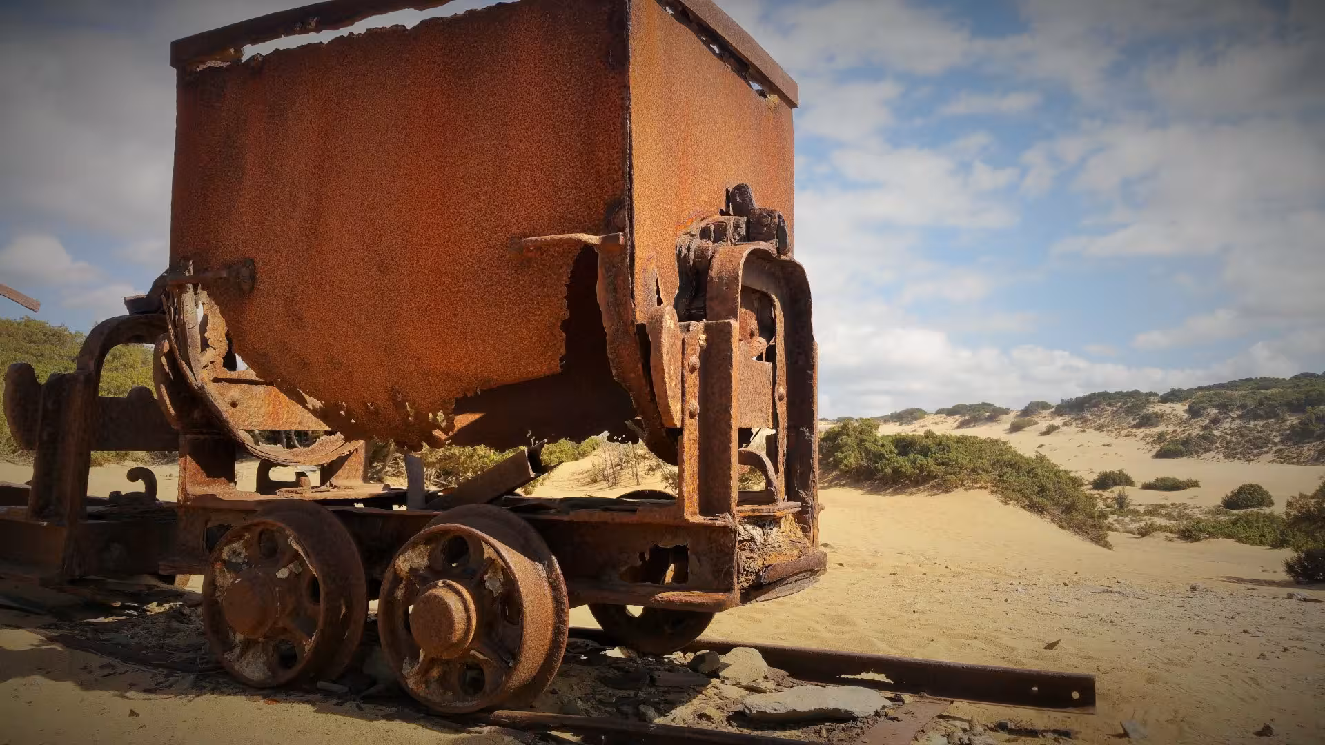 Rustic mining cart in the sandy landscape of Piscinas, highlighting Sardinia's rich industrial history.