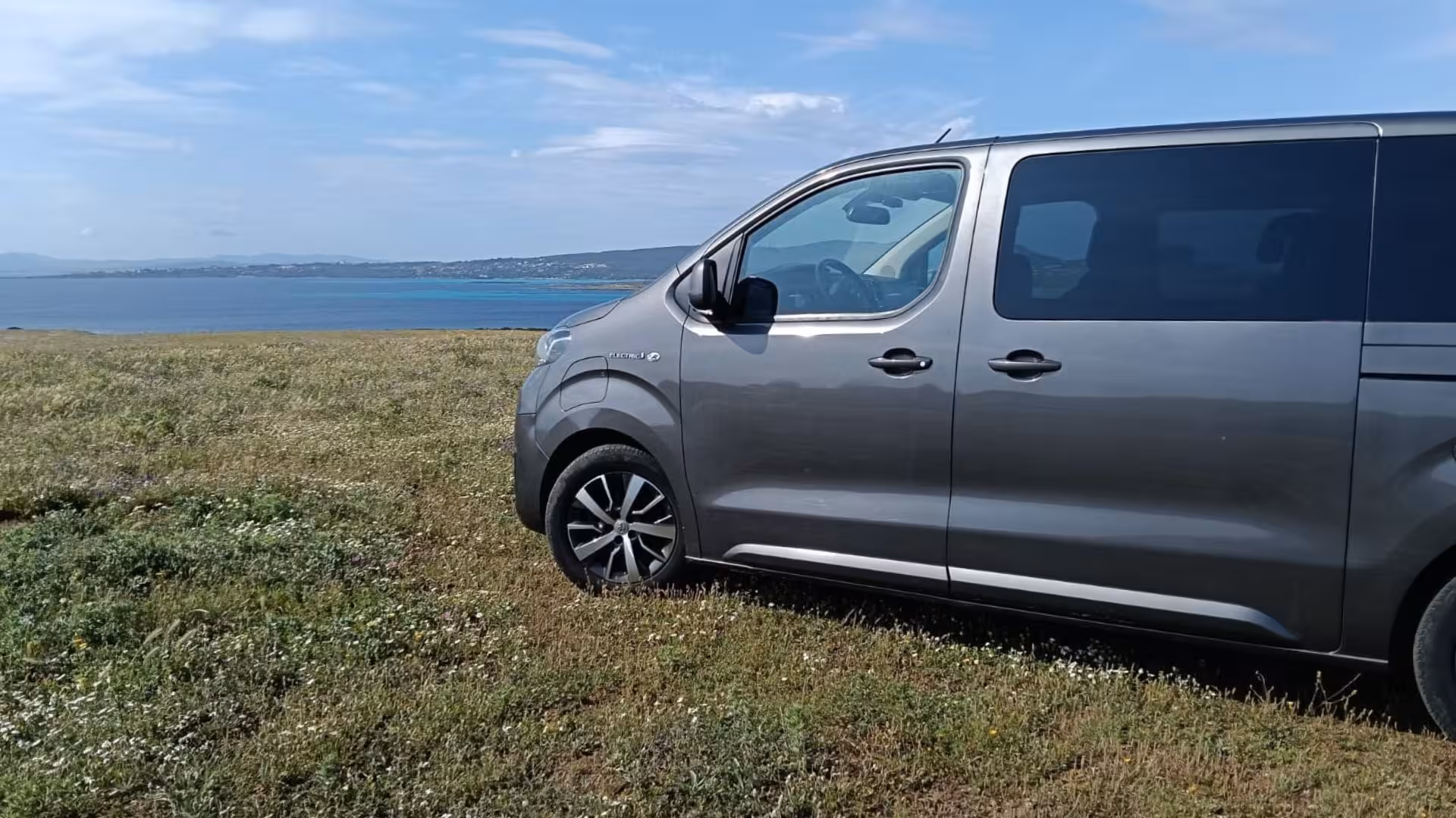 Modern minivan parked on grassy Asinara Island overlooking the stunning coastline, featured in Porto Torres tour.