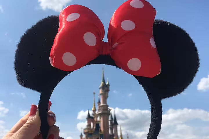 Minnie Mouse ears headband held up in front of Disneyland Paris castle under blue sky