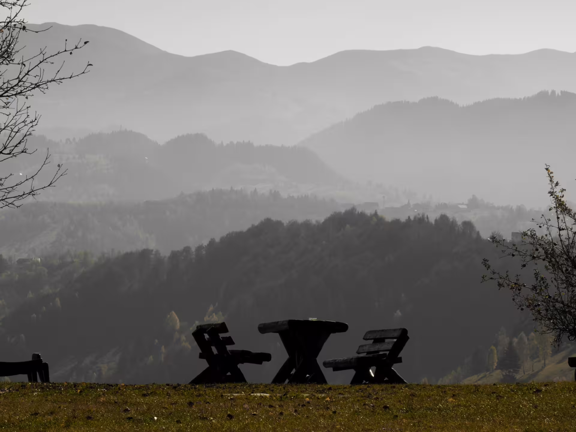 Wooden picnic table and chairs silhouetted against misty layered mountain valleys in rural Romania