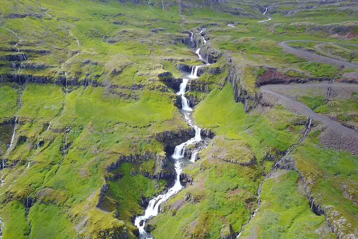 Aerial view of cascading waterfalls flowing through lush green cliffs in Mjoifjordur Fjord, East Iceland