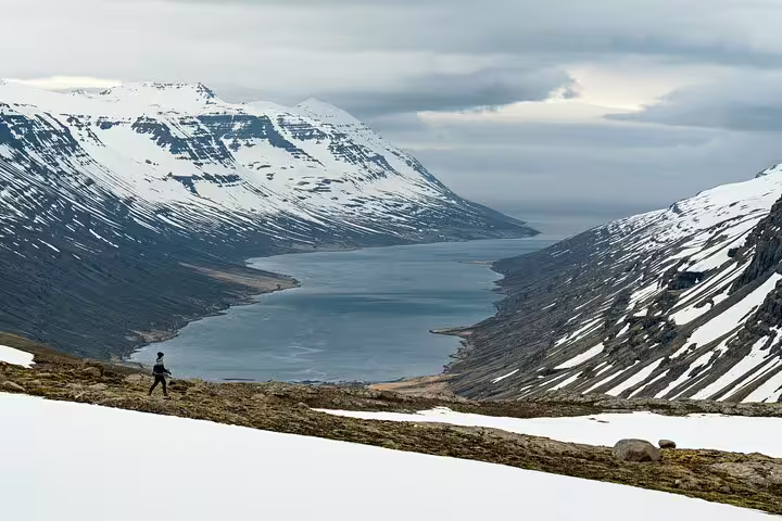 Hiker overlooking Mjoifjordur fjord surrounded by snow-capped mountains in East Iceland