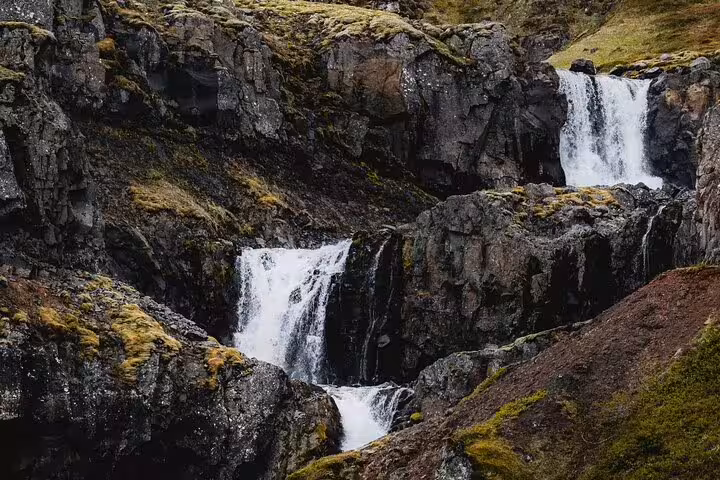 Cascading multi-tiered waterfall over dark volcanic rock cliffs with moss in Mjoifjordur, East Iceland