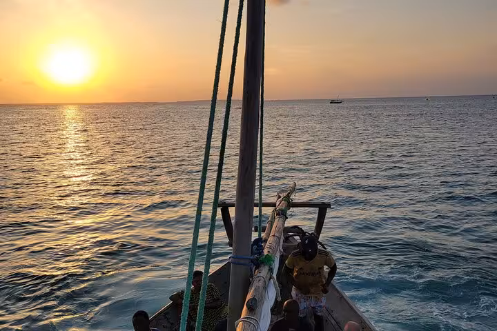 Traditional dhow sailing at sunset on Mnemba Island, part of the Zanzibar dolphin and snorkeling tour.