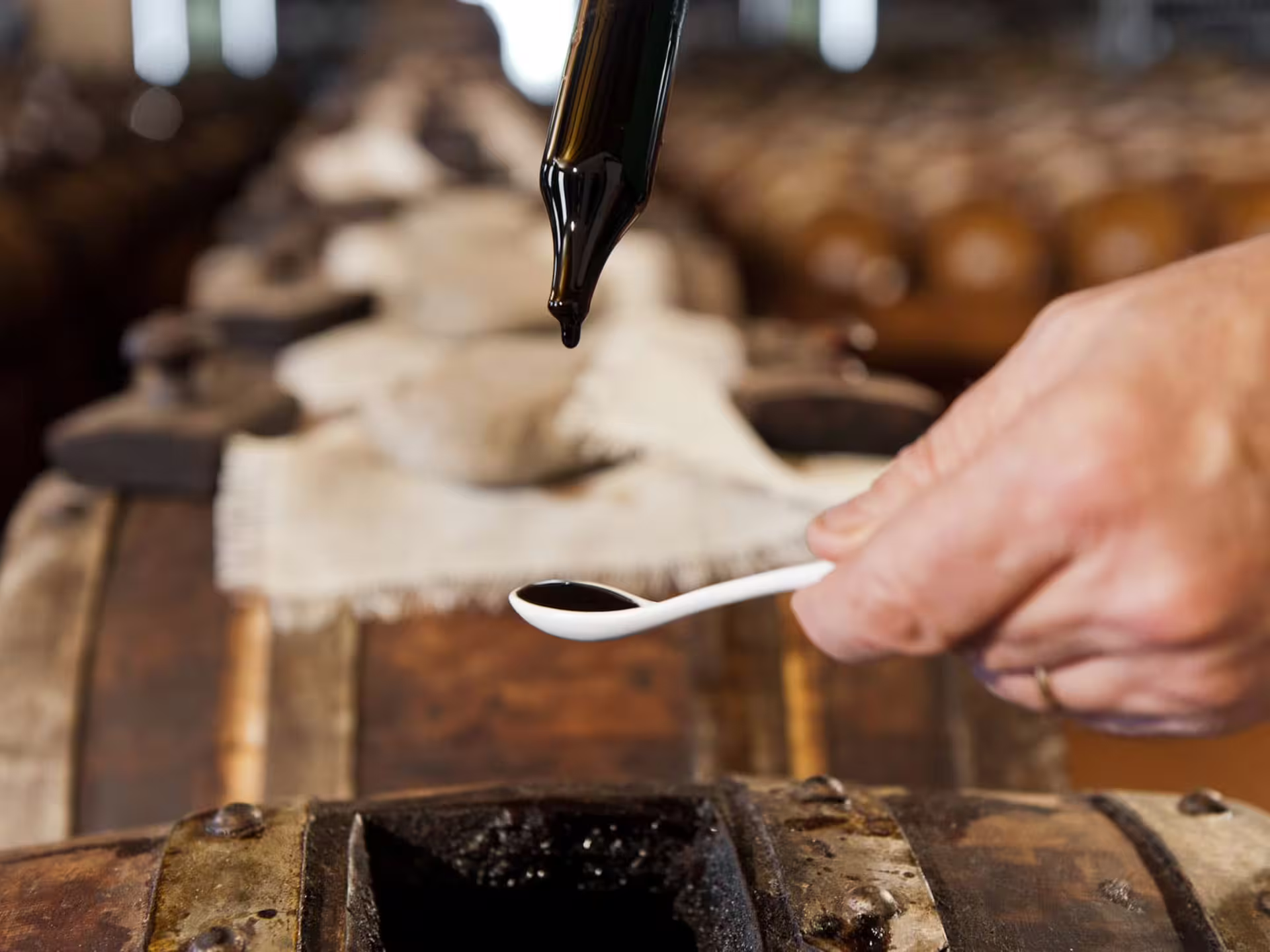 Traditional balsamic vinegar tasting in Modena with a close-up of a spoon capturing rich, aged flavors from a barrel.