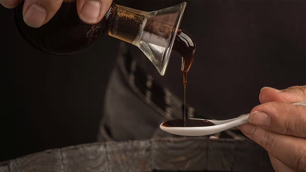 Pouring traditional balsamic vinegar into a tasting spoon during Modena vinegar cellar tour with aperitif