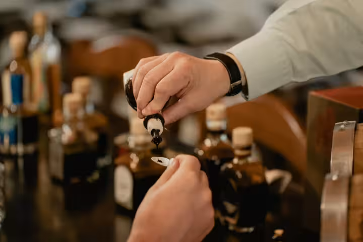 Close-up of a hand pouring rich balsamic vinegar into a tasting spoon, highlighting Modena's authentic flavors.