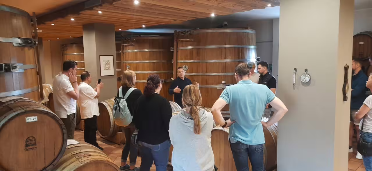 Tour group exploring balsamic vinegar barrels in Modena's traditional aging cellar.