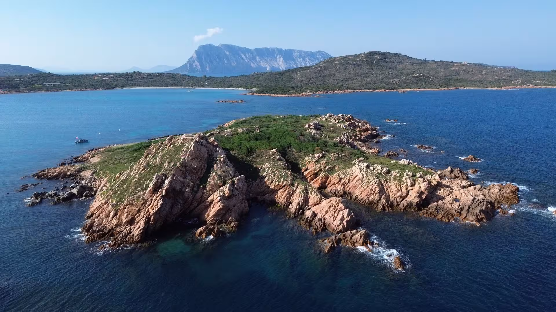 Scenic view of rocky Molara Island with lush greenery and turquoise waters in the foreground.