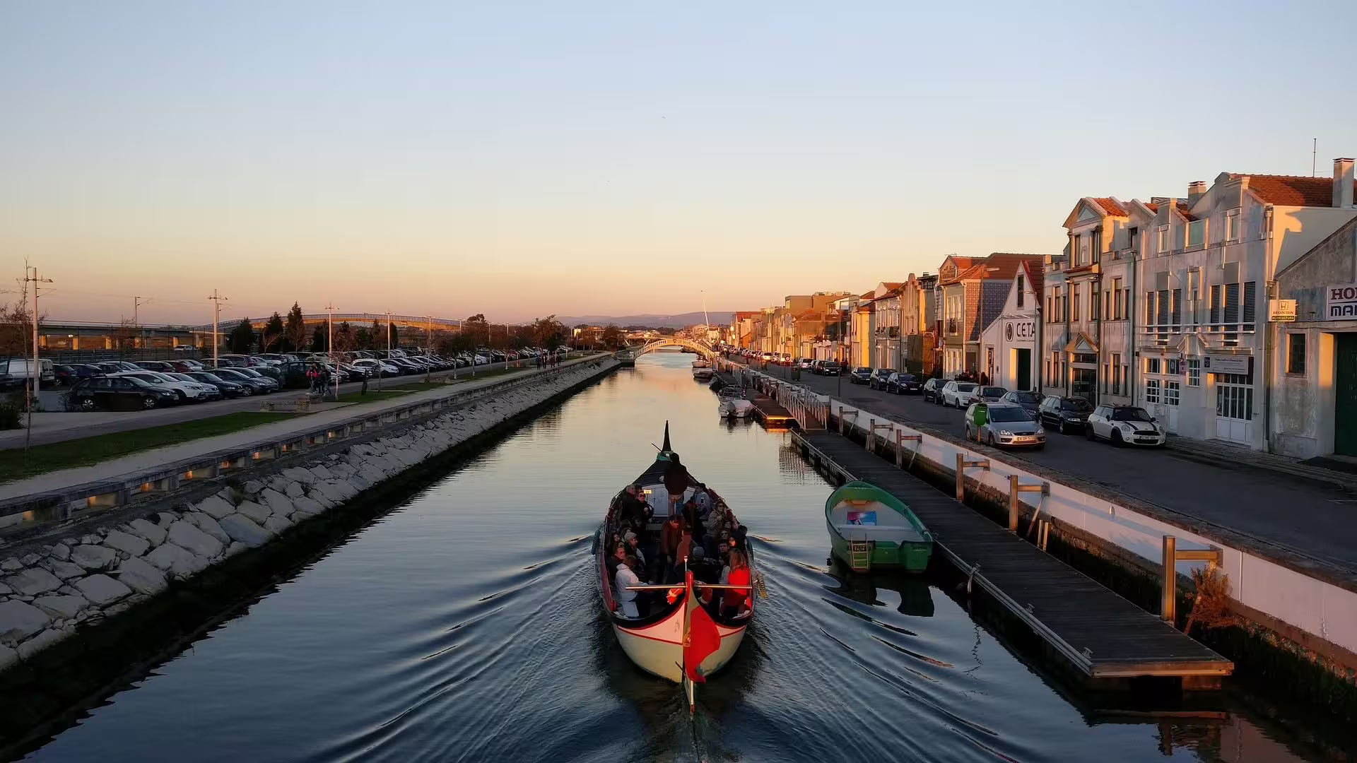 Moliceiro boat glides through Aveiro canal at sunset, offering a serene view of the city's charming architecture.