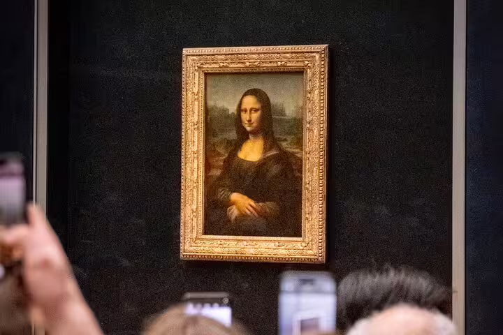 Close-up of the Mona Lisa painting surrounded by visitors capturing photos at the Louvre Museum.