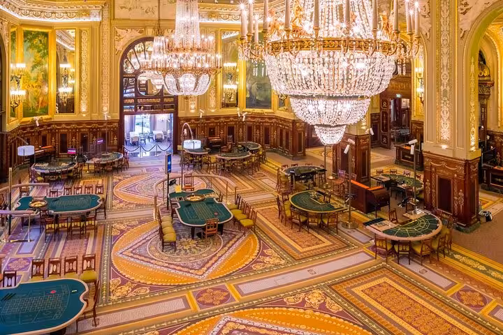 Ornate casino gaming room in Monaco with crystal chandeliers, green felt tables, and gilded décor