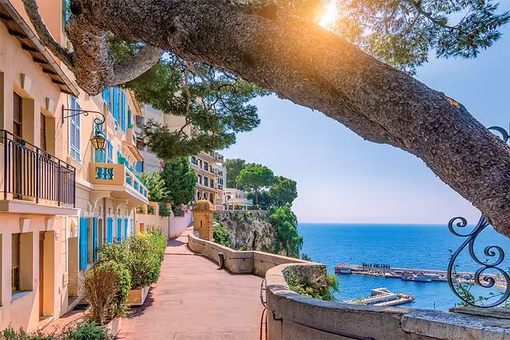 Scenic coastal promenade in Monaco with pastel buildings, blue shutters, and Mediterranean sea views