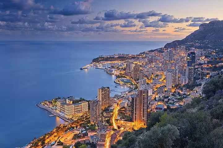 Aerial twilight view of Monaco's coastline with illuminated city skyline and Mediterranean Sea