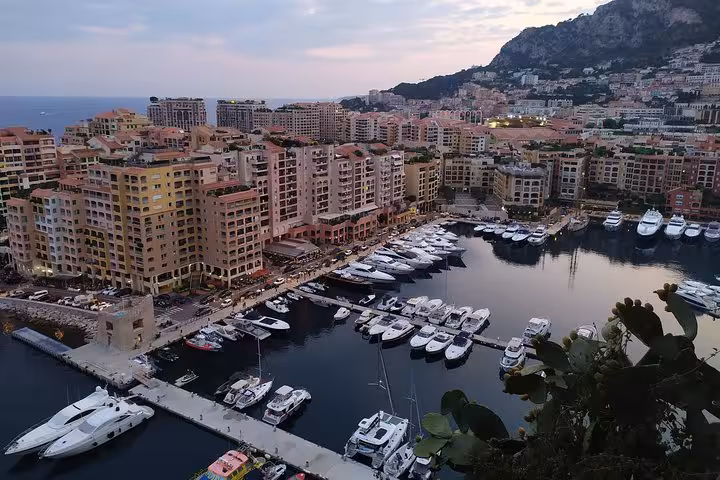 Monaco harbor at dusk with luxury yachts and illuminated waterfront buildings overlooking the Mediterranean Sea