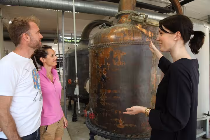 Guide explaining copper distillery equipment to two tourists on a Monaco Eze tour from Nice