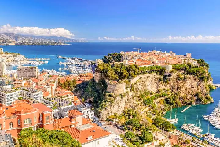 Aerial view of Monaco's rocky coastline with terracotta rooftops, marina with yachts, and blue Mediterranean Sea