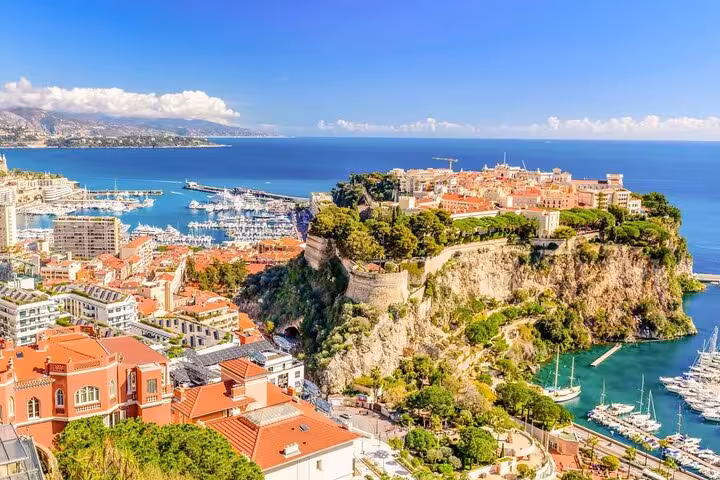 Aerial view of Monaco's rocky peninsula with orange-roofed buildings, luxury yacht harbor, and Mediterranean Sea