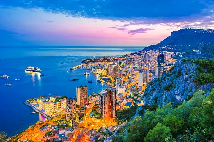 Aerial twilight view of Monaco cityscape with illuminated streets, harbor, cruise ship, and Mediterranean Sea