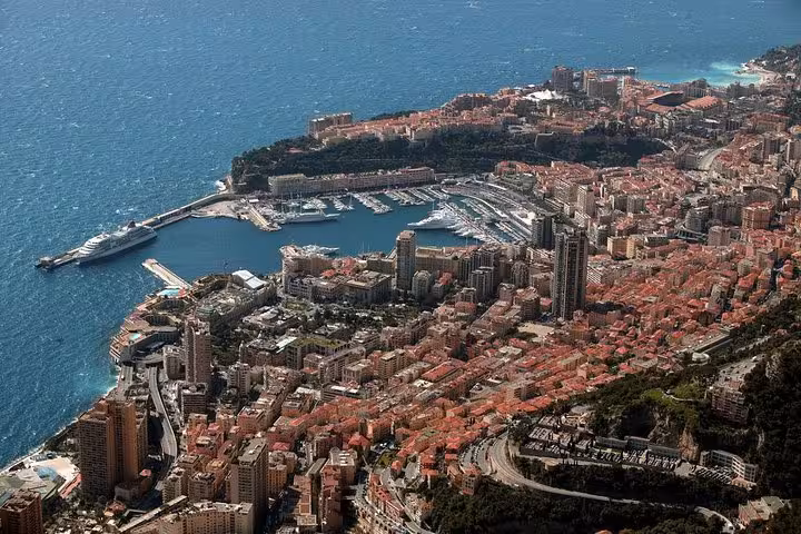 Aerial view of Monaco harbor with luxury yachts, dense city buildings, and Mediterranean coastline