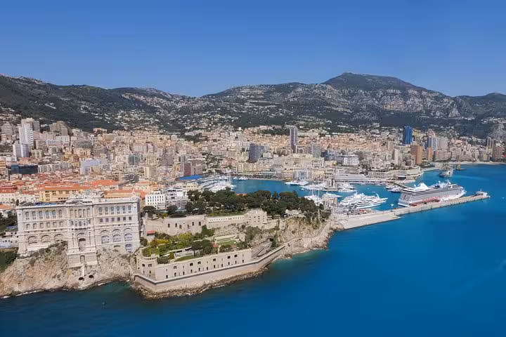 Aerial view of Monaco coastline with turquoise harbor, luxury yachts, and dense cityscape backed by mountains