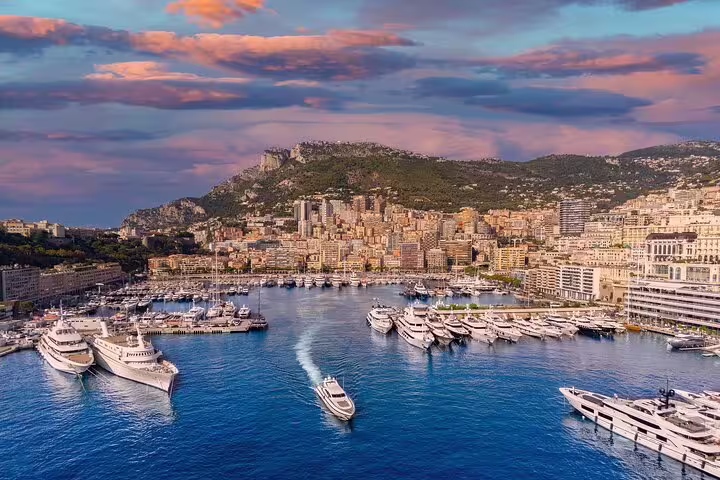 Aerial view of Monaco harbor with luxury yachts, dense cityscape, and rocky hillside at sunset