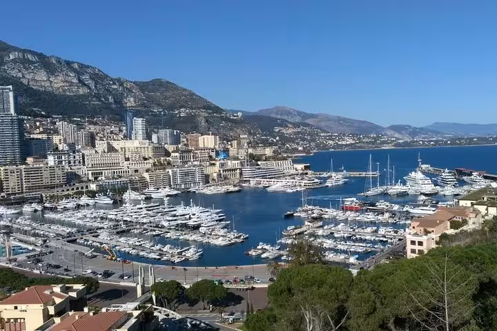 Aerial view of Monaco harbor filled with luxury yachts, city buildings, and mountains in the background
