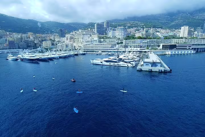 Aerial view of Monaco harbor with luxury yachts, marina, and city skyline against cloudy mountains