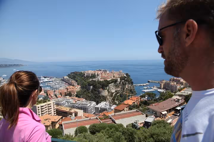 Tourists overlooking Monaco's harbor, Prince's Palace rock, and Mediterranean coastline from a scenic viewpoint