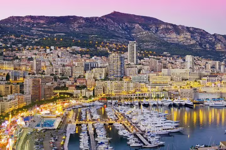 Panoramic twilight view of Monaco harbor with luxury yachts, city buildings, and mountain backdrop