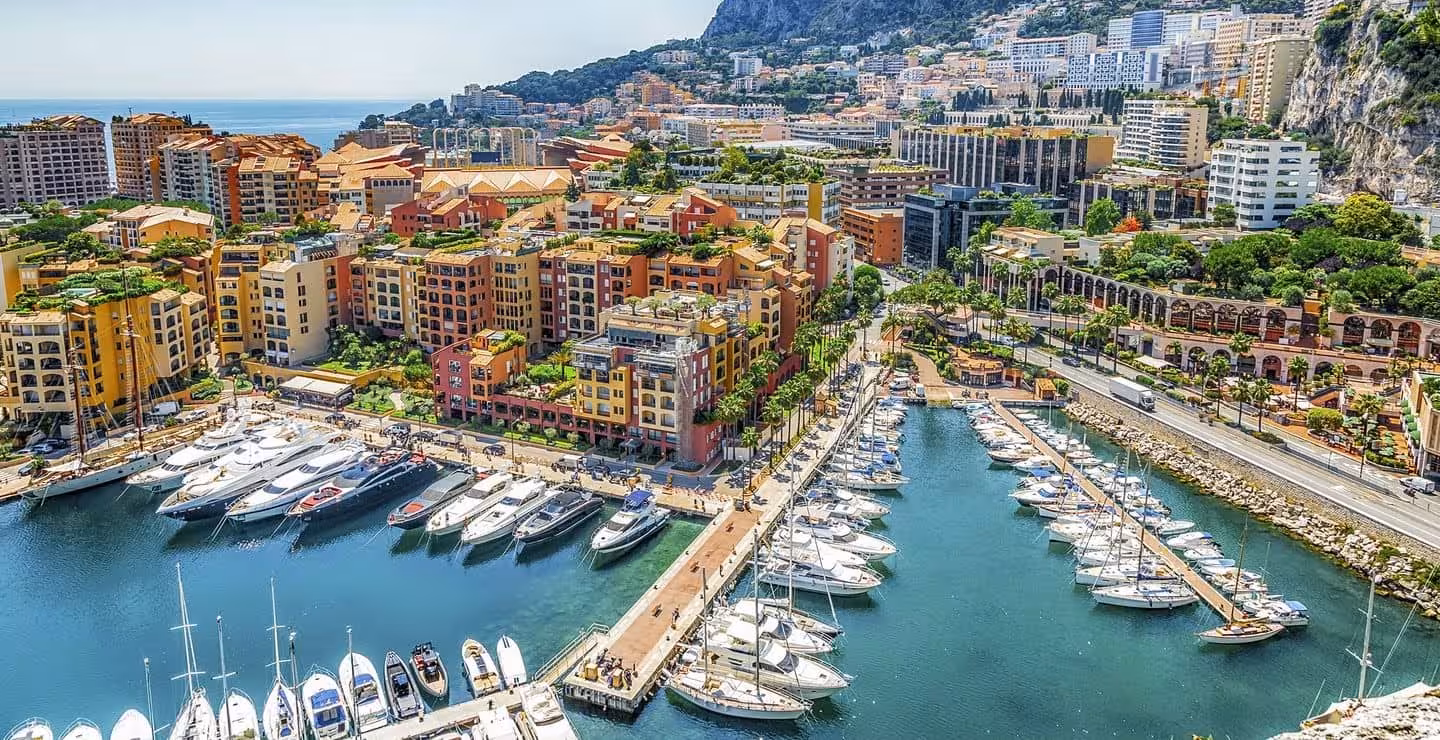 Aerial view of Monaco marina with luxury yachts, colorful buildings, and Mediterranean coastline on a sunny day