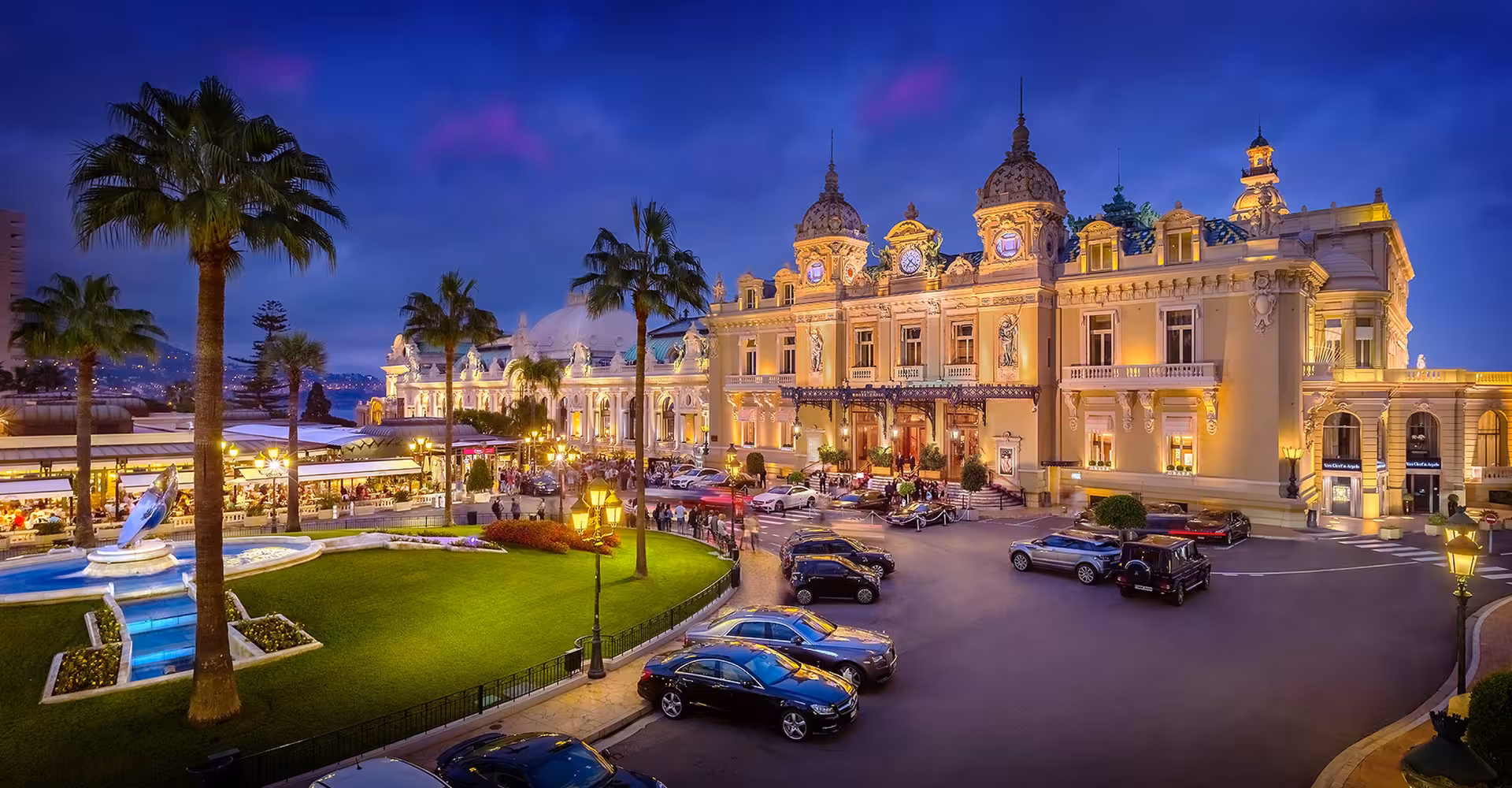 Monte Carlo Casino illuminated at night with luxury cars and palm trees in Monaco