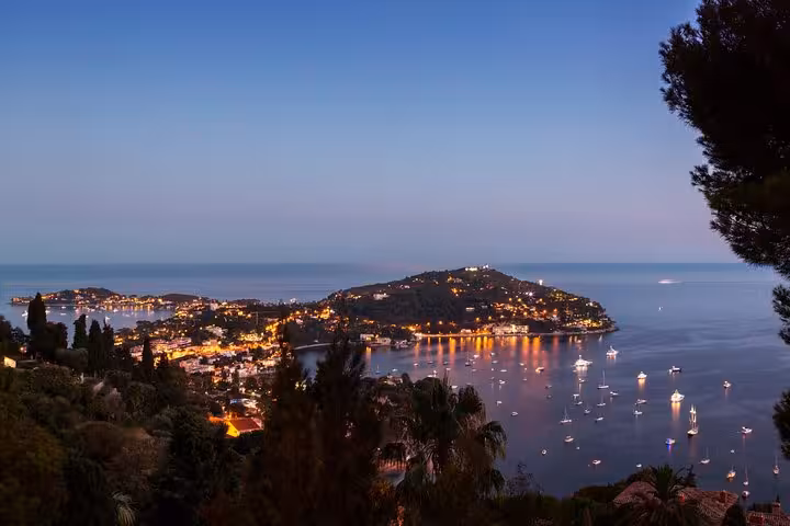 Enchanting view of Monte-Carlo coastline at dusk with twinkling lights reflecting on the serene Mediterranean Sea.