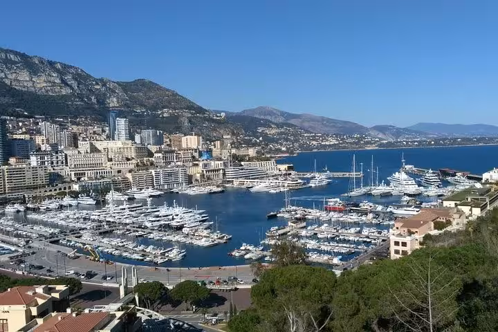 Aerial view of Monaco harbor filled with luxury yachts, city buildings, and Mediterranean coastline backed by mountains