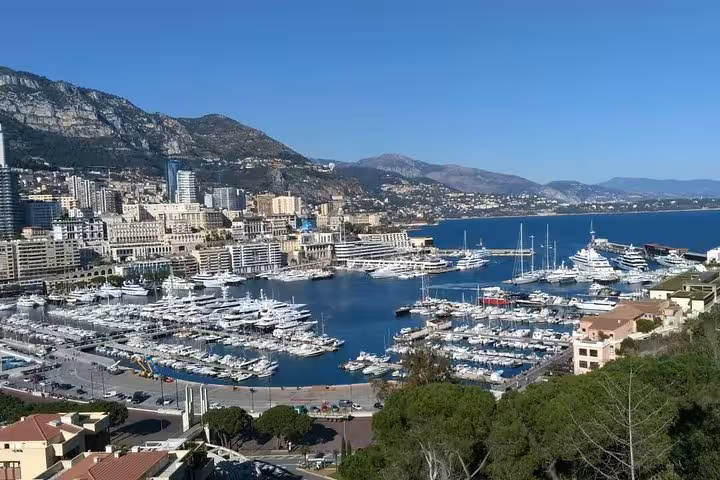 Aerial view of Monaco harbor filled with luxury yachts, city buildings, and mountains in the background