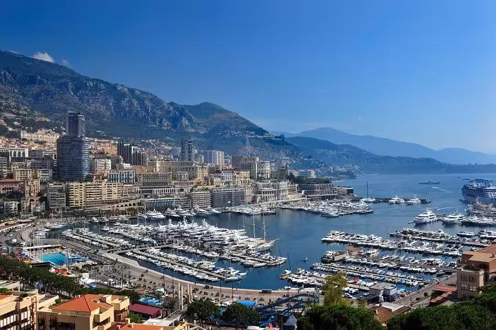 Panoramic view of Monaco harbor with luxury yachts, city buildings, and mountain backdrop on a sunny day