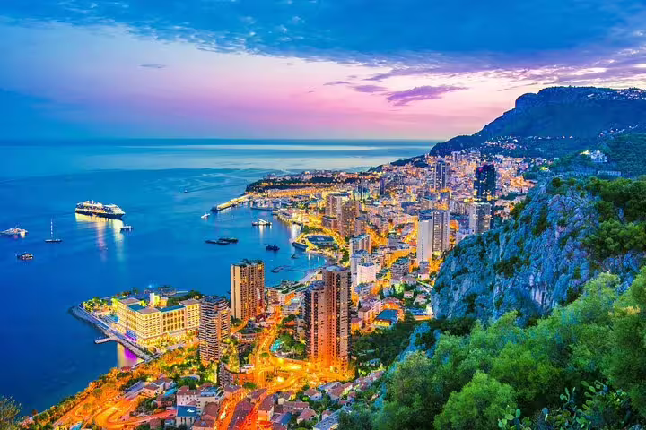 Aerial panoramic view of Monaco cityscape at twilight with glittering lights, harbor, cruise ship, and Mediterranean Sea