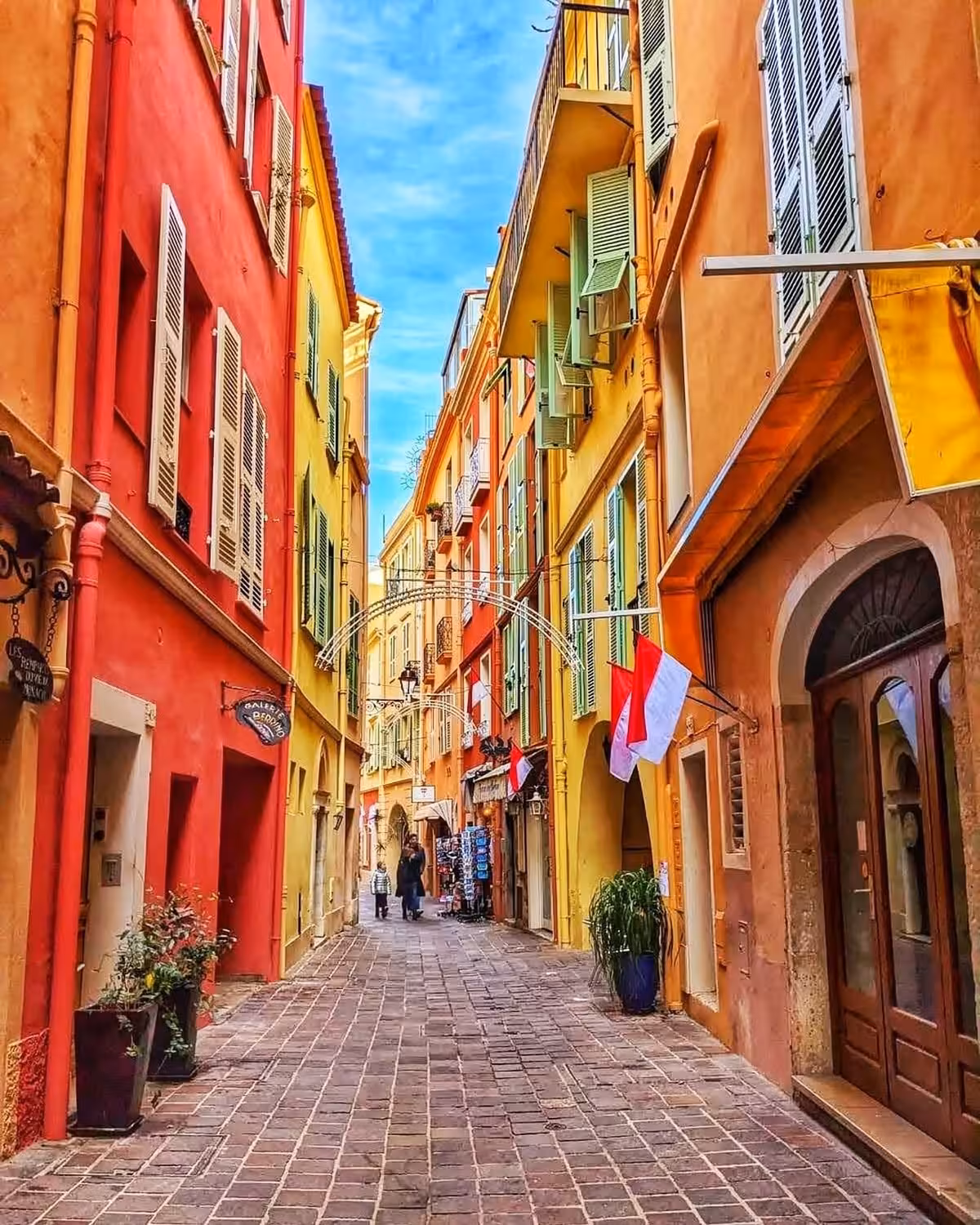 Colorful narrow cobblestone street in Monaco's old town with red and yellow buildings and Monegasque flags