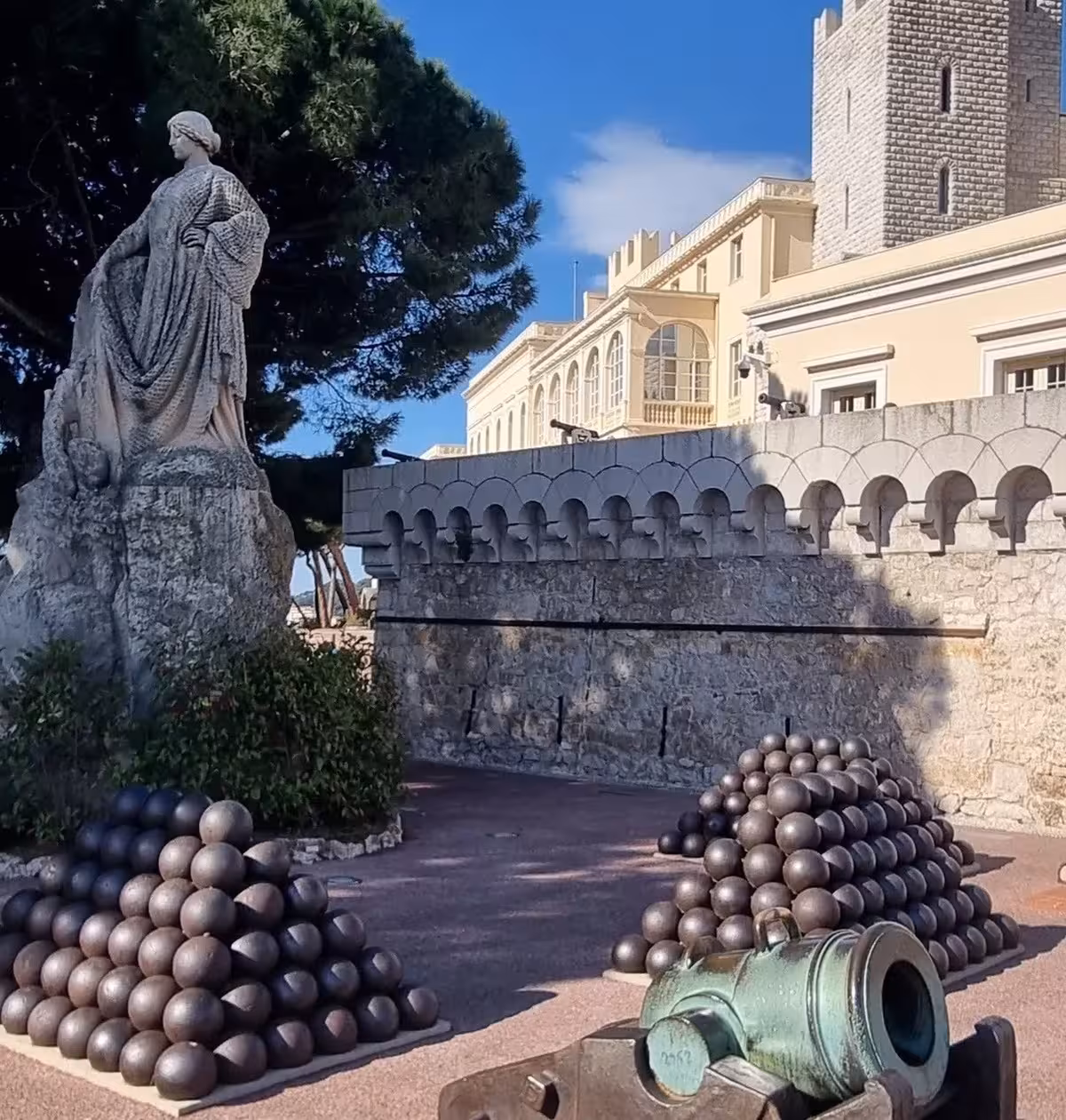 Cannons and cannonballs outside Monaco Prince's Palace with a stone statue and fortress walls