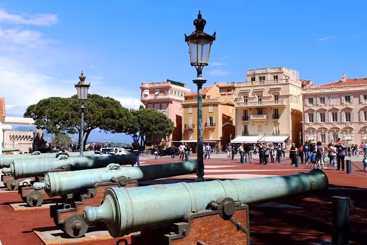 Historic bronze cannons at Monaco Palace Square with colorful buildings and tourists on French Riviera