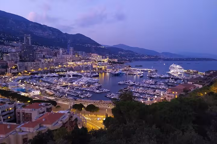 Monaco harbor illuminated at dusk with luxury yachts and cruise ship, city lights reflecting on calm water