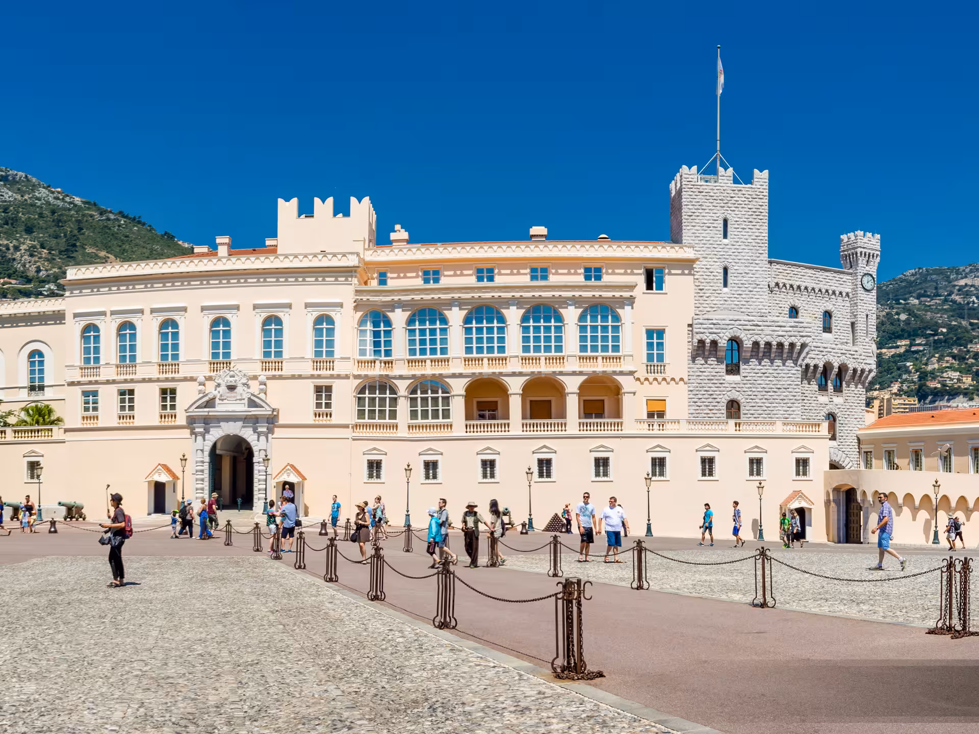Prince's Palace of Monaco courtyard with tourists on a sunny day, featuring medieval towers and elegant facades