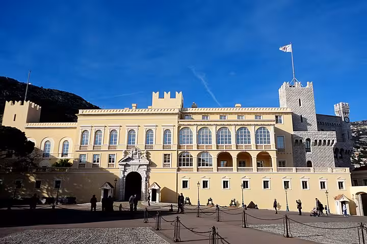 Prince's Palace of Monaco courtyard with yellow facade, battlements, and flag under blue sky