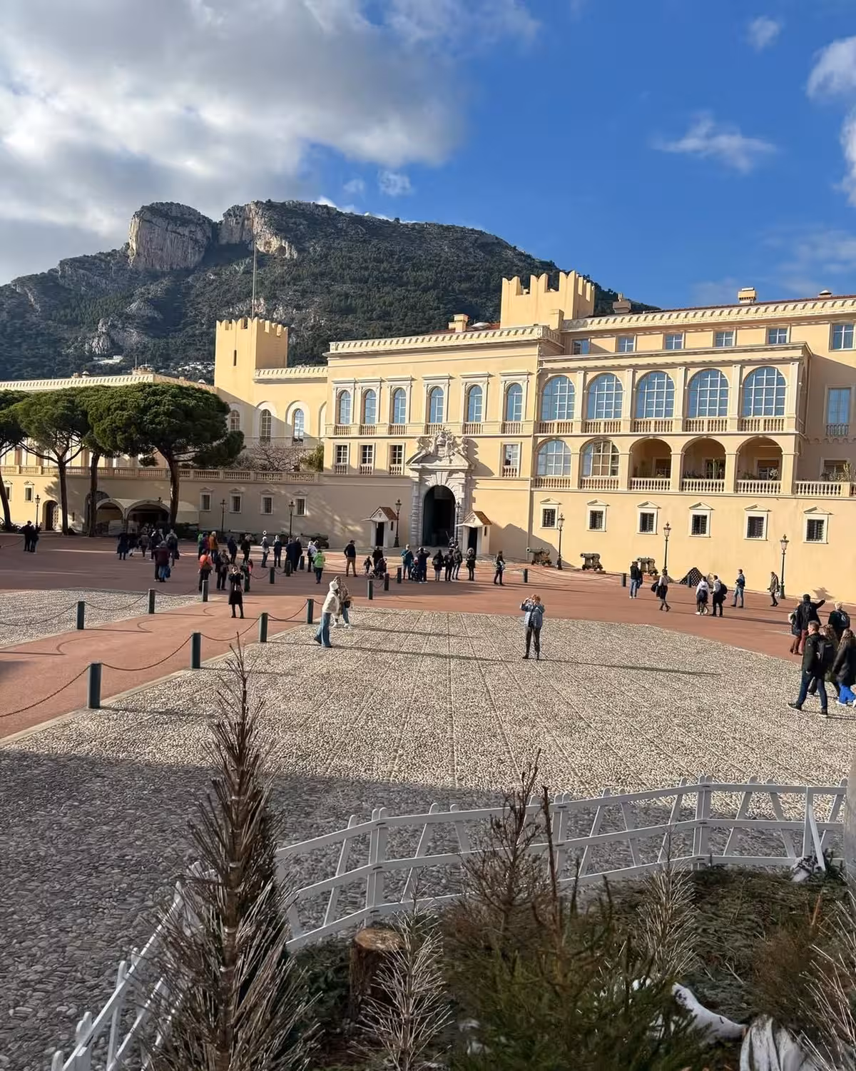 Prince's Palace of Monaco courtyard with tourists and rocky mountain backdrop on sunny day