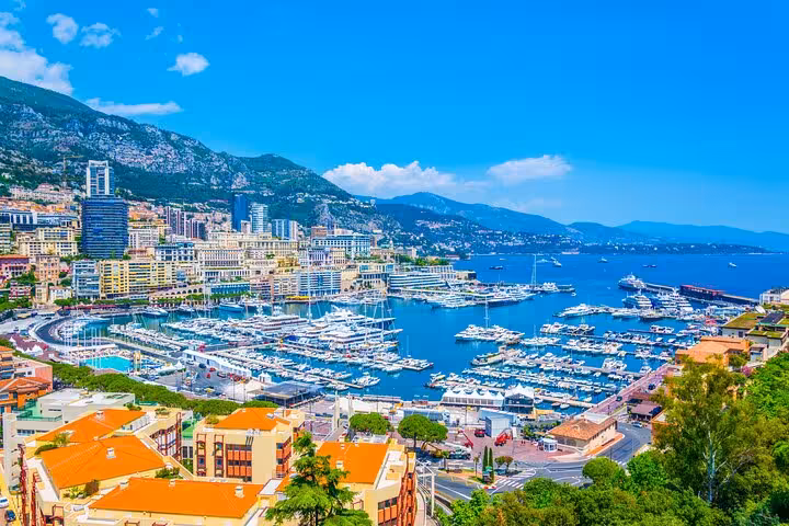 Panoramic view of Monaco's luxurious marina with yachts, set against a backdrop of mountains and azure waters.