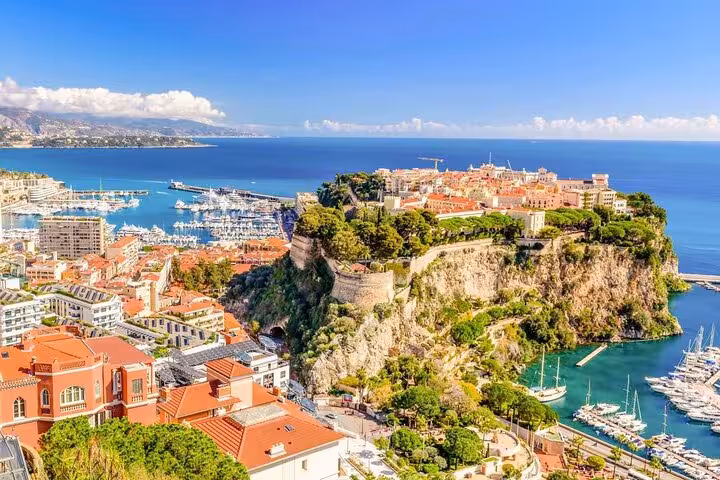 Aerial view of Monaco's historic rock fortress, harbor with yachts, and terracotta rooftops along the French Riviera coastline