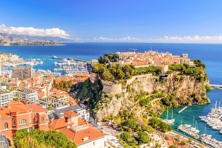 Panoramic view of Monaco's iconic Rock with luxury yachts, turquoise harbor, and terracotta rooftops on the French Riviera.