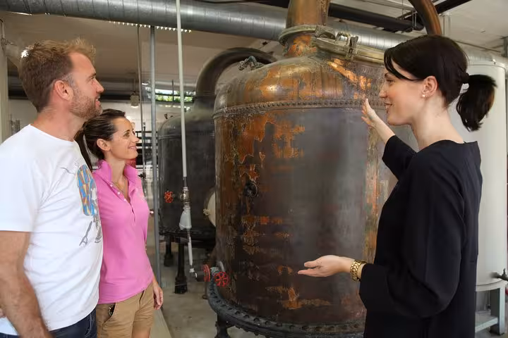 Tour guide explaining copper distillery equipment to two visitors at a facility near Monaco