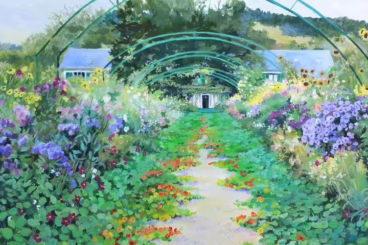 Flower-lined garden path with green arched trellises leading to Monet's house in Giverny